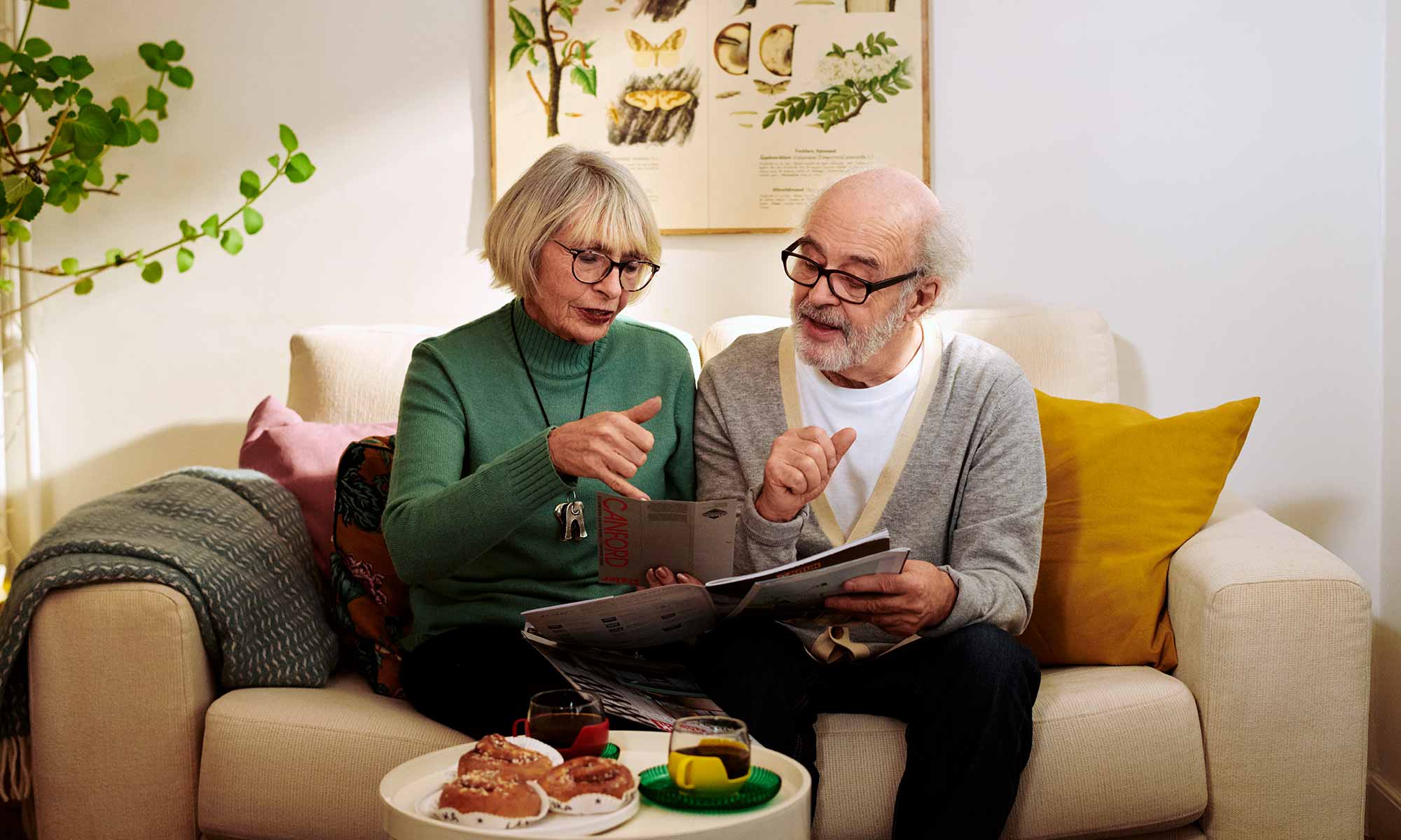 Äldre par sitter hemma i soffan och tittar i en bok