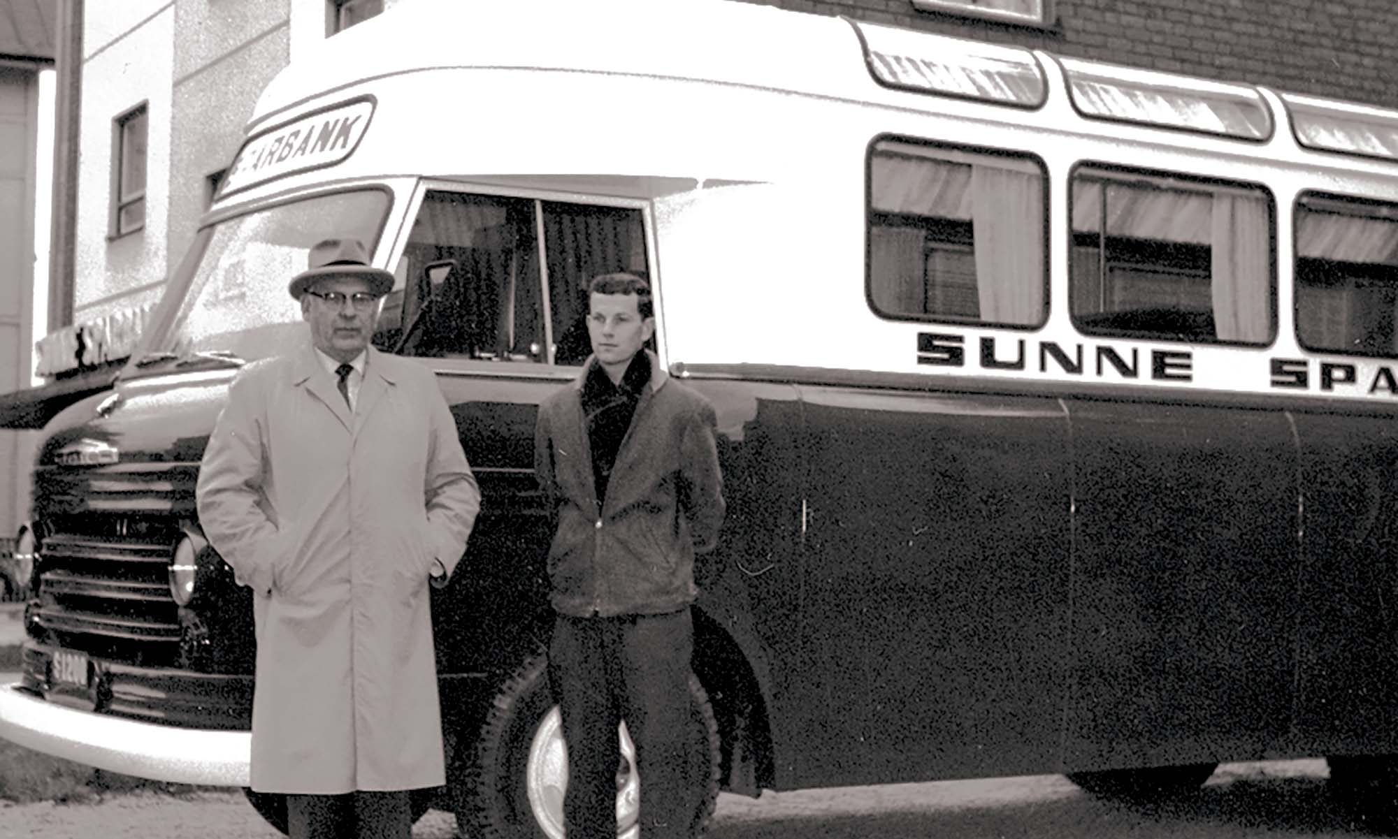 Svartvitt foto av två män framför en buss på 1960-talet.