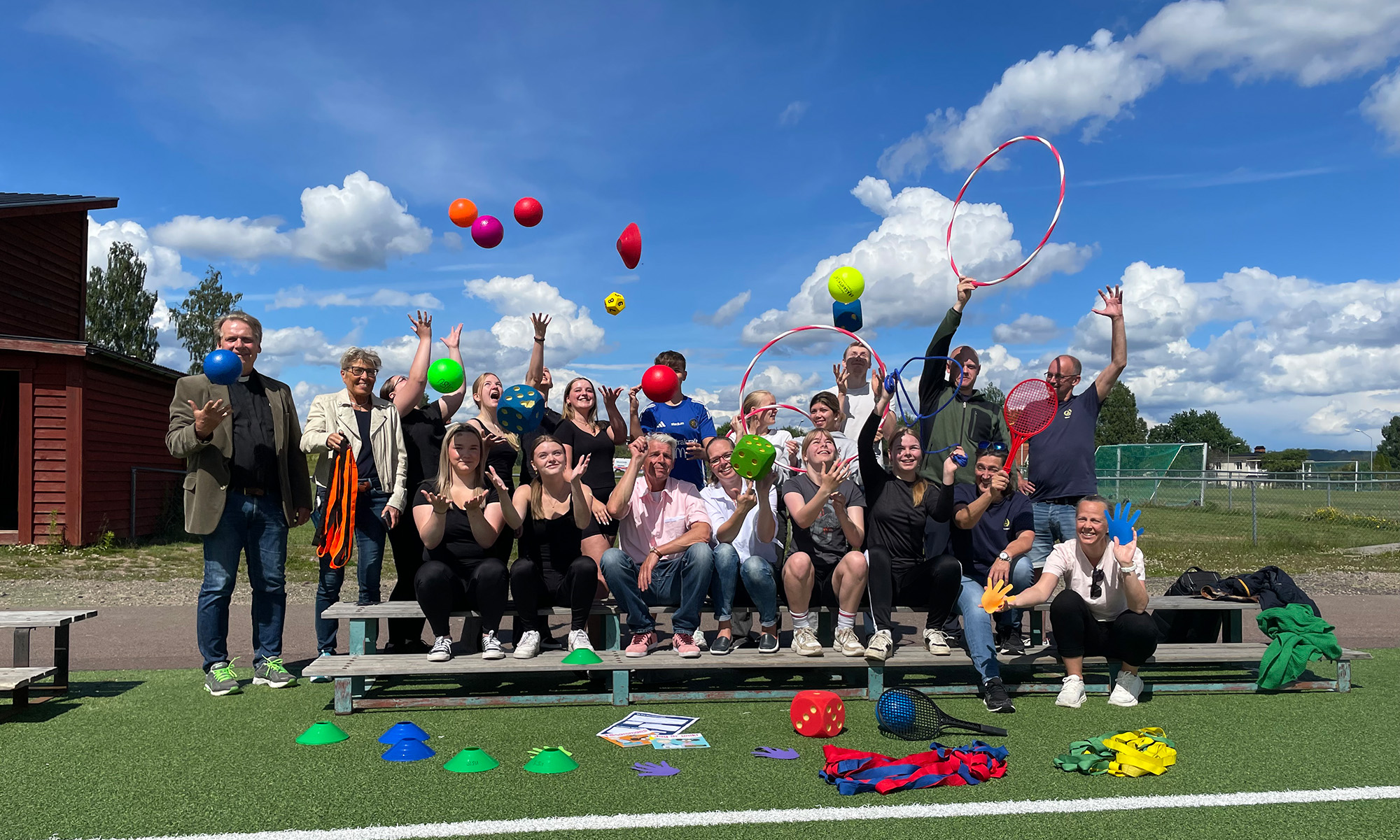 En stor grupp människor i olika åldrar kastar bollar i luften på en fotbollsplan.